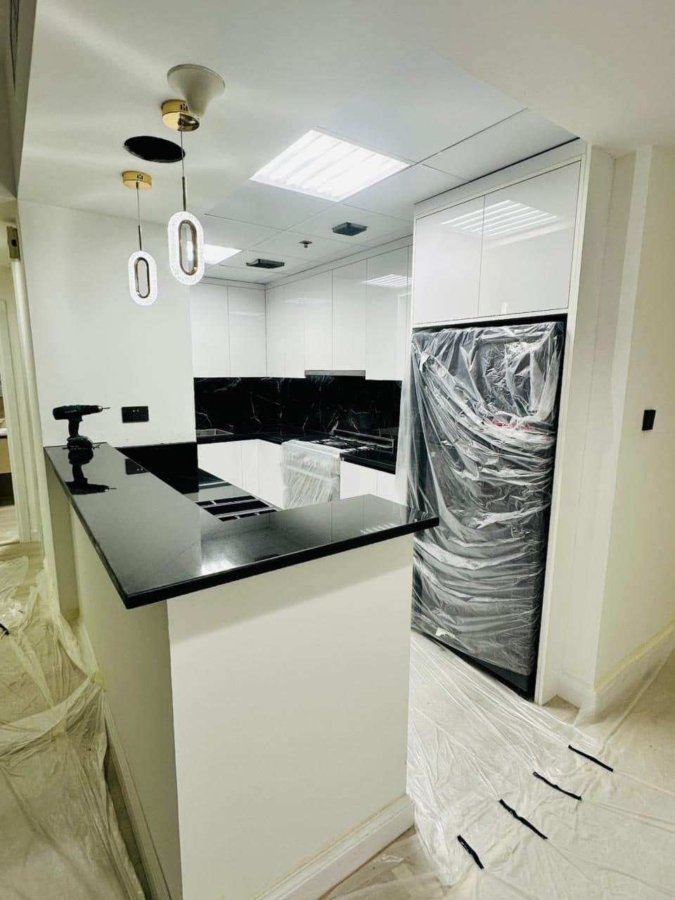 Black stone countertop and cabinetry mid-fit-out, with appliances still wrapped for protection and floor sheeting down during the build.