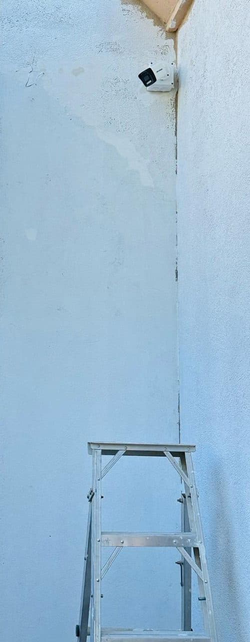 Dome CCTV camera mounted on an exterior stucco wall corner, angled to cover the approach to the property.