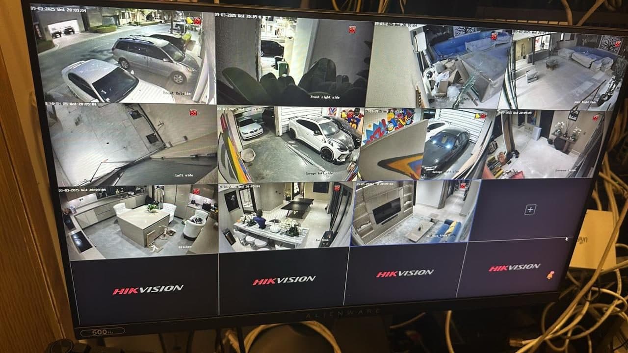 CCTV monitor showing a 12-camera split-screen view covering a property's exterior, garage, kitchen and living areas.
