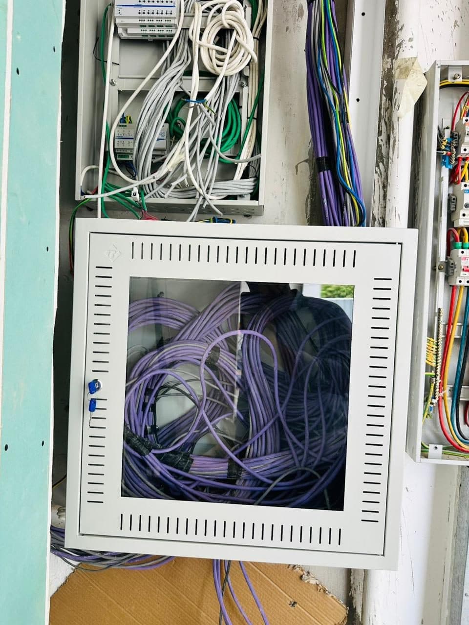Electrical distribution board with colour-coded circuit breakers installed in a wall cavity alongside a structured cabling cabinet.