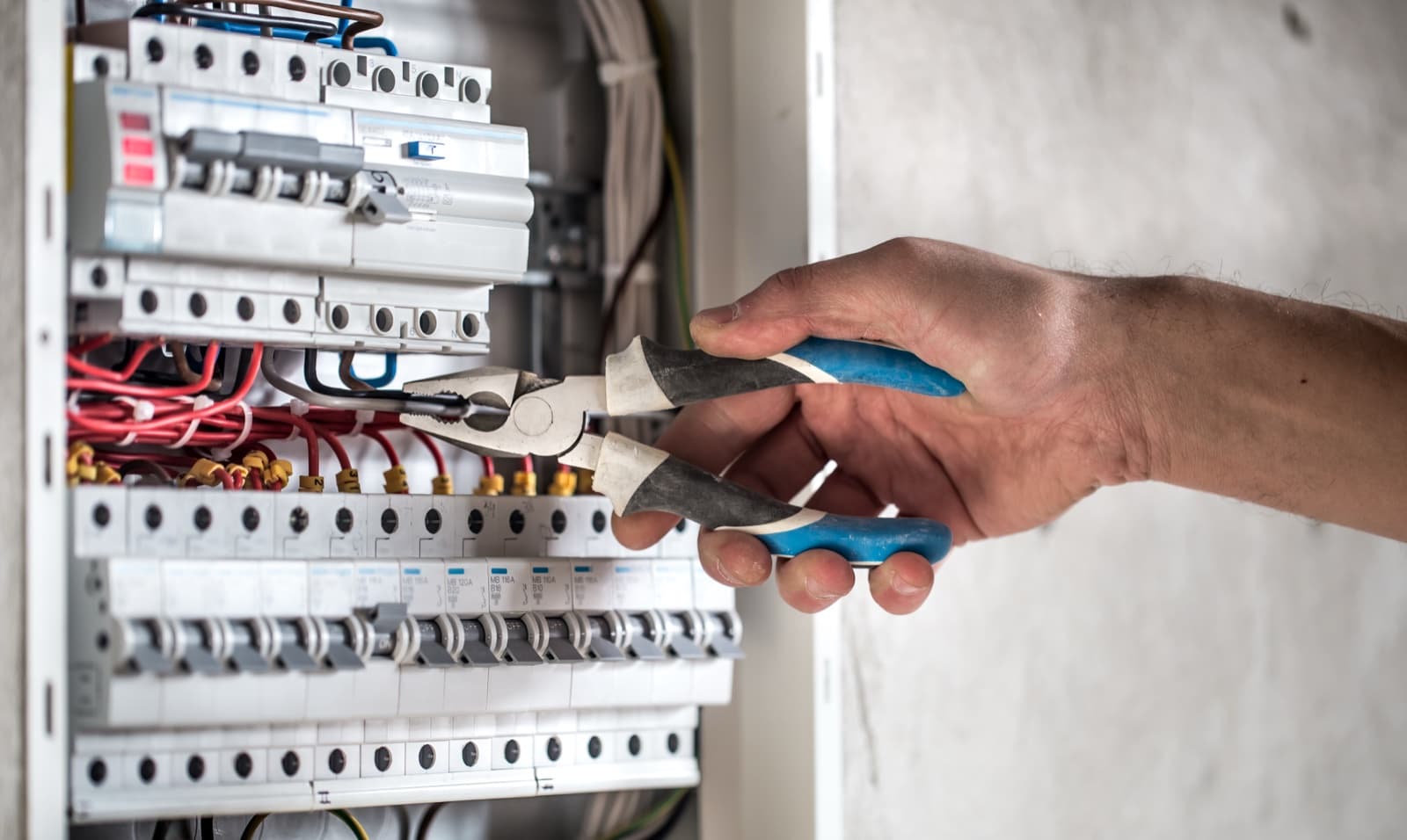 Electrician using pliers to work on wiring inside an open circuit breaker panel