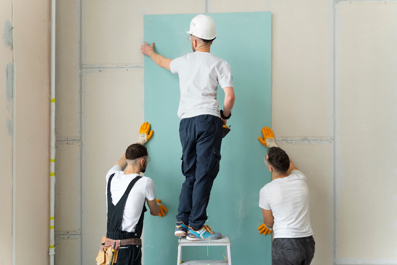 Three-person team lifting a gypsum board panel into place for a partition wall